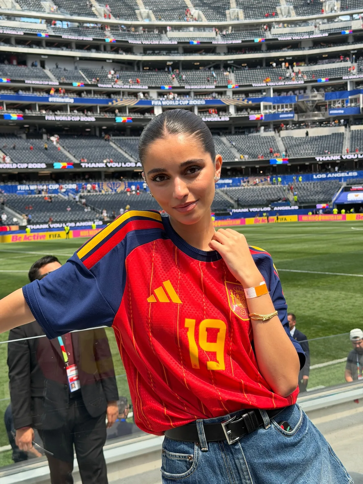 Inés García Santos pozuje na trybunach stadionu w koszulce reprezentacji Hiszpanii. Influencerka zestawiła sportowy T-shirt z jeansami i czarnym paskiem.