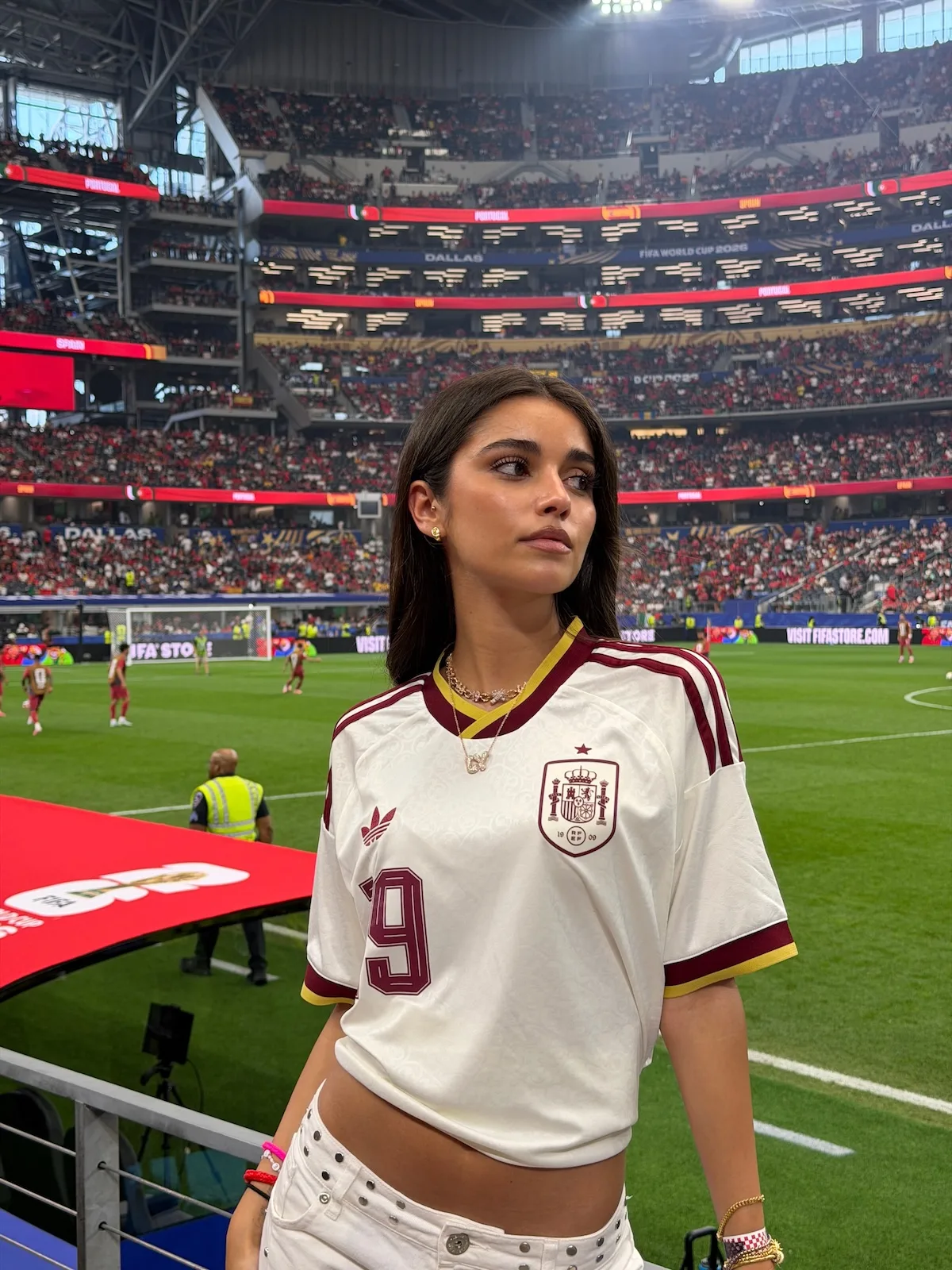 Inés García Santos pozuje przy murawie stadionu w białej koszulce reprezentacji Hiszpanii z numerem 19. Influencerka uzupełniła sportową stylizację białymi jeansami i złotą biżuterią.