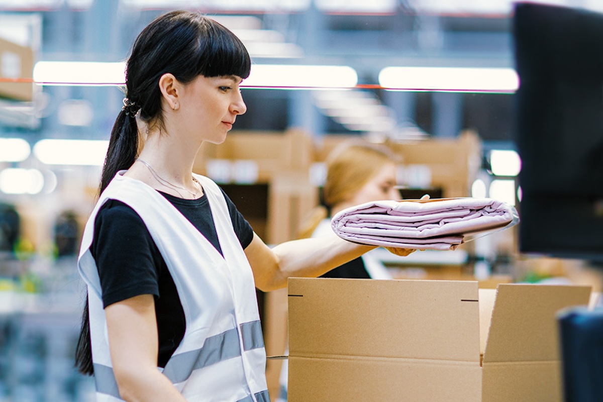 LPP Logistics otwiera nowy magazyn w Rumunii pod Bukaresztem. Na zdjęciu kobieta pracująca w magazynie LPP, wkładająca ubrania do kartonowego pudełka.