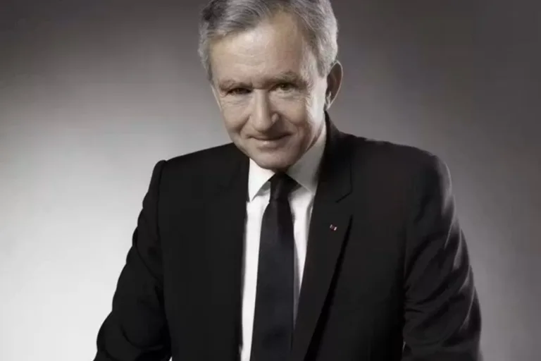 Sukcesja w LVMH. Bernard Arnault w czarnym garniturze, białej koszuli i czarnym krawacie pozuje na szarym, studyjnym tle. Prezes LVMH patrzy w stronę aparatu i lekko się uśmiecha.