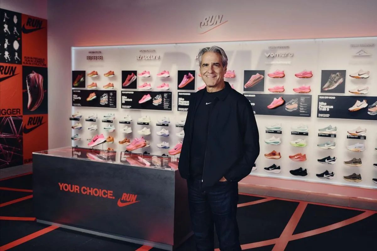Zarobki prezesów firm modowych. Elliott Hill, prezes Nike, stoi w przestrzeni ekspozycyjnej marki na tle ściany wypełnionej modelami butów sportowych. Menedżer ubrany jest w ciemną kurtkę i koszulkę z logo Nike. W 2025 roku znalazł się na czele rankingu najlepiej opłacanych prezesów branży mody i handlu.