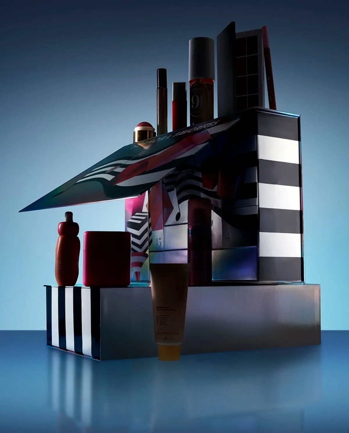 Kalendarz adwentowy Sephora Favorites 2026 z kolorowymi szufladkami i kosmetykami ustawionymi wokół opakowania. Na zdjęciu widać produkty do makijażu, pielęgnacji i perfumy na niebieskim tle.
