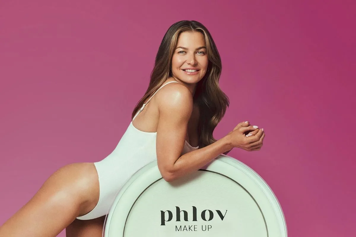 Anna Lewandowska sprzeda udziały we Phlov? Na zdjęciu Anna Lewandowska pozuje w białym body na różowym tle, opierając się o duże opakowanie z logo Phlov Make Up.