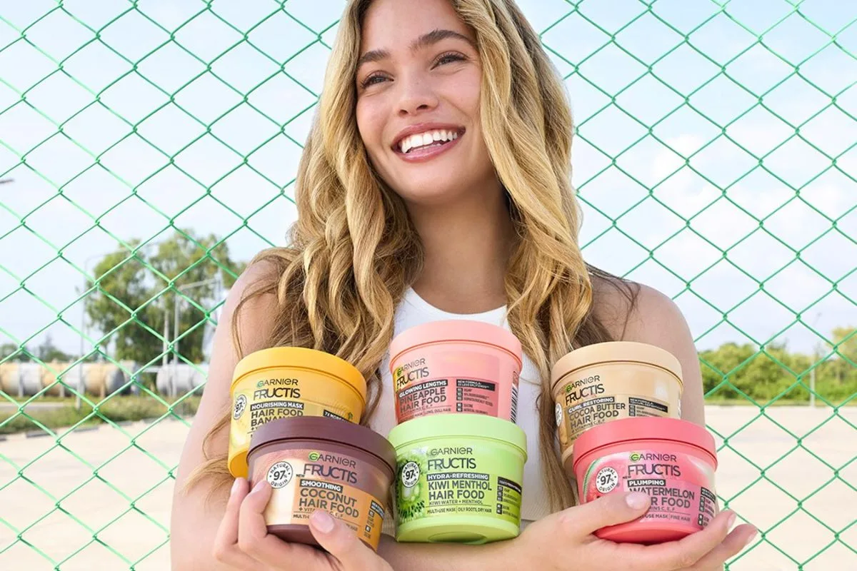 UOKiK kontra L’Oréal Polska i kosmetyki Garnier. Kobieta trzyma opakowania kosmetyków Garnier Fructis Hair Food na tle zielonej siatki.