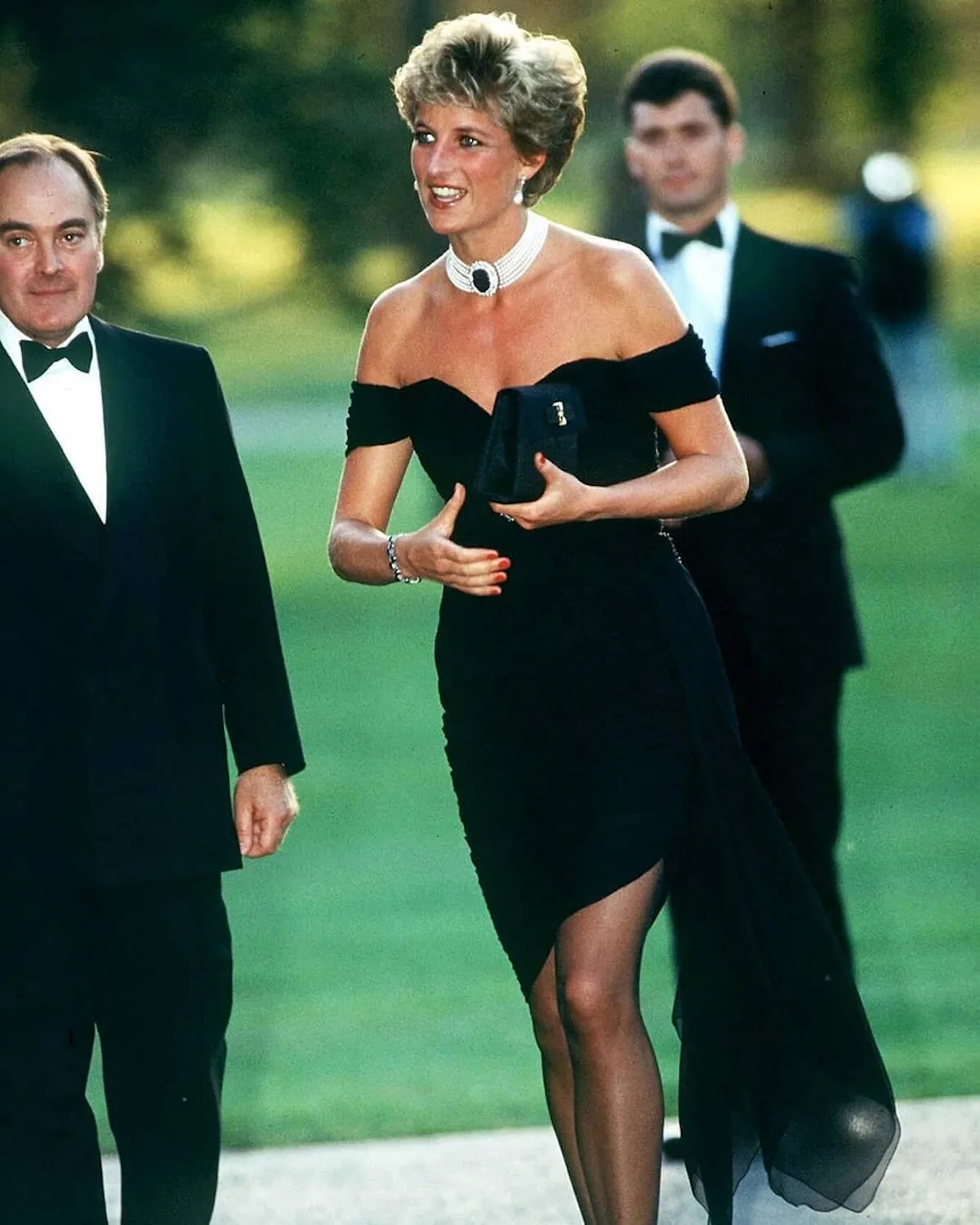 Księżna Diana w słynnej czarnej „revenge dress” podczas przyjęcia w Serpentine Gallery w 1994 roku. Ma na sobie sukienkę z odkrytymi ramionami, perłowy naszyjnik z ciemnym kamieniem i trzyma czarną kopertówkę.