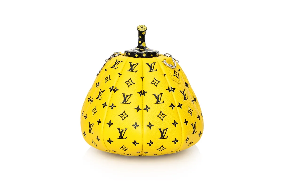 Żółta torebka Louis Vuitton x Yayoi Kusama w kształcie dyni, ozdobiona czarnym monogramem LV i kontrastowym ogonkiem w kropki, sfotografowana na białym tle.