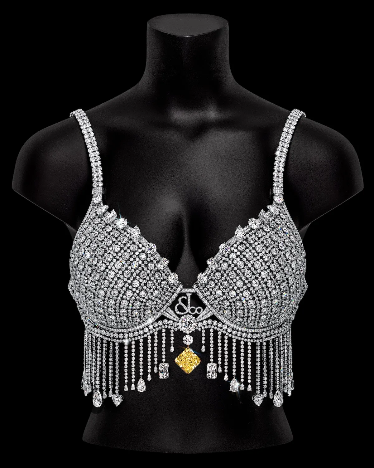 Fantasy Bra Victoria’s Secret wysadzany diamentami na czarnym manekinie – widok z przodu, z ozdobnymi diamentowymi frędzlami i dużym żółtym diamentem pośrodku.