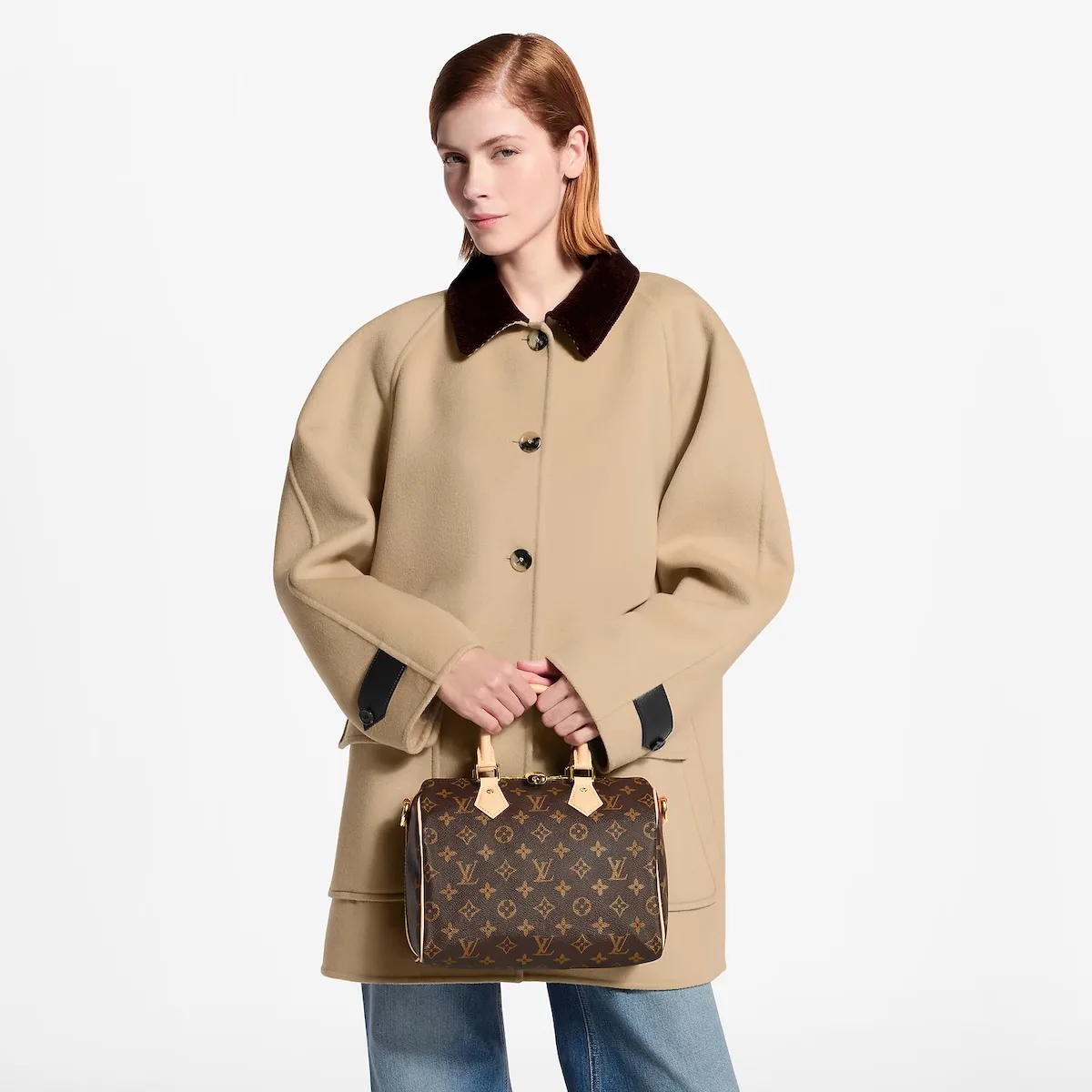 Modelka w beżowym płaszczu trzyma brązową torebkę Louis Vuitton Speedy z charakterystycznym monogramem i jasnymi skórzanymi uchwytami.