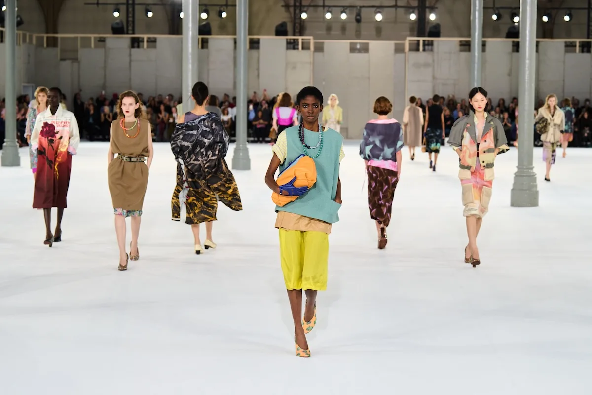 Pokaz Dries Van Noten wiosna–lato 2027. Modelki prezentują kolorowe stylizacje, a na pierwszym planie widać miętowy top, żółte bermudy i pomarańczową torbę.