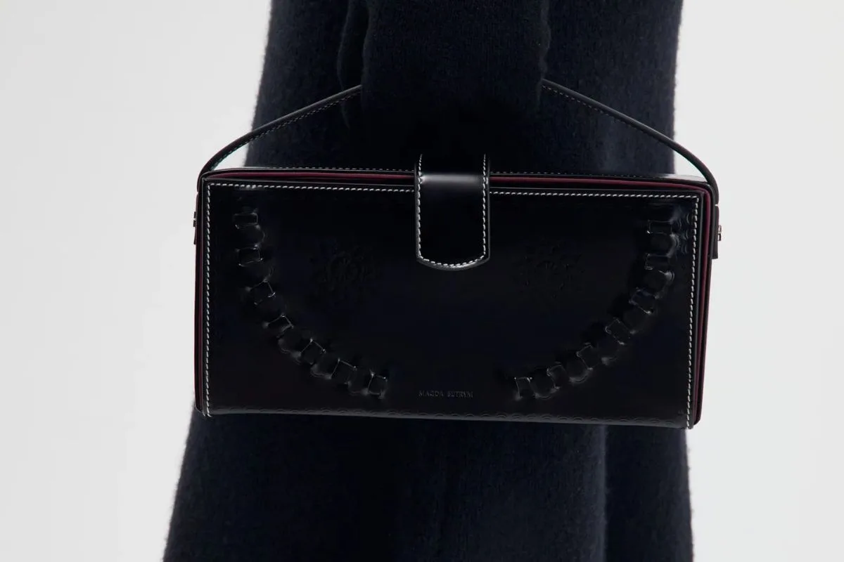 Czarna skórzana torebka Magdy Butrym o prostokątnym kształcie, ozdobiona subtelnymi tłoczeniami i dekoracyjnymi przeszyciami. Model z kolekcji Podhale Leather ma krótką rączkę i kontrastowe jasne szwy.