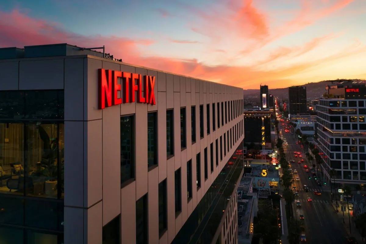 Netflix zwolnienia 2026. Na zdjęciu siedziba Netflixa w Los Angeles z dużym, czerwonym logo na fasadzie budynku. W tle widać miejskie wieżowce, ulicę oraz niebo o zachodzie słońca.