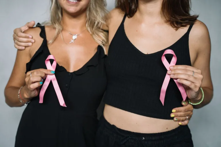 Dwie kobiety w czarnych ubraniach obejmują się i trzymają różowe wstążki – symbole solidarności i profilaktyki raka piersi podczas Różowego Października 2026.